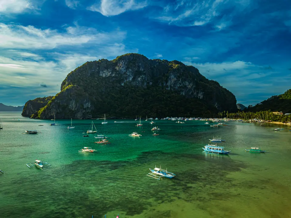 Aerial view of El Nido, Palawan showing dramatic limestone karst cliffs, turquoise Bacuit Bay waters, scattered outrigger boats and a tropical…