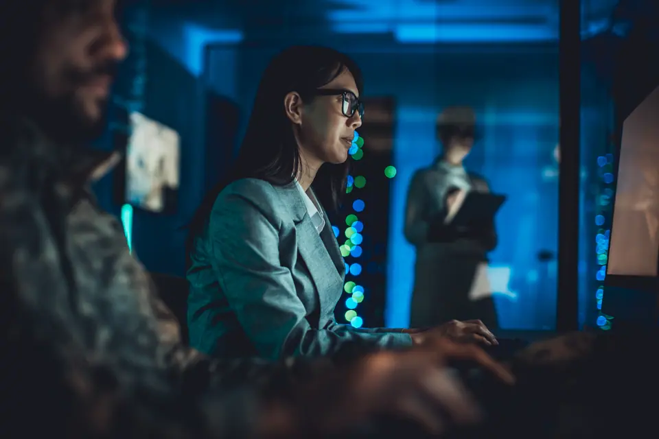Asian woman using computer and monitoring systems in modern data center with colleagues working in background
