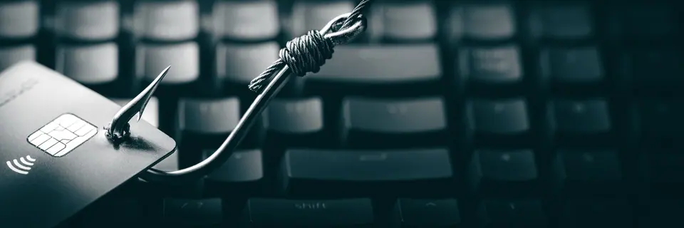 Credit card and large fish hook on computer keyboard background - cybercrime/phishing concept