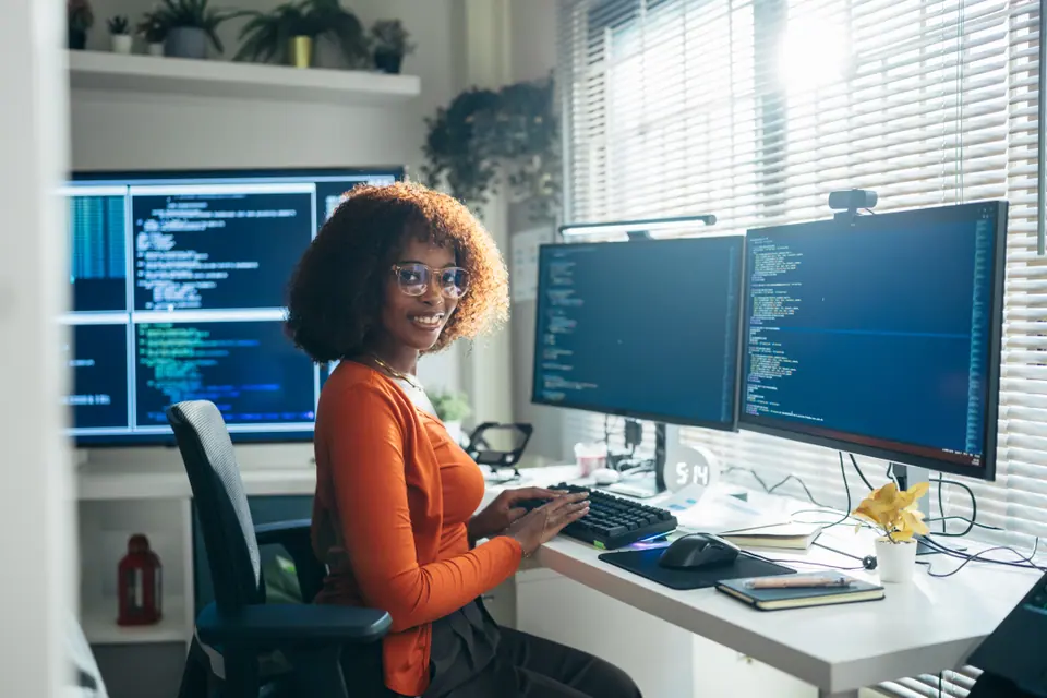 Female software developer coding at multi-monitor computer workstation