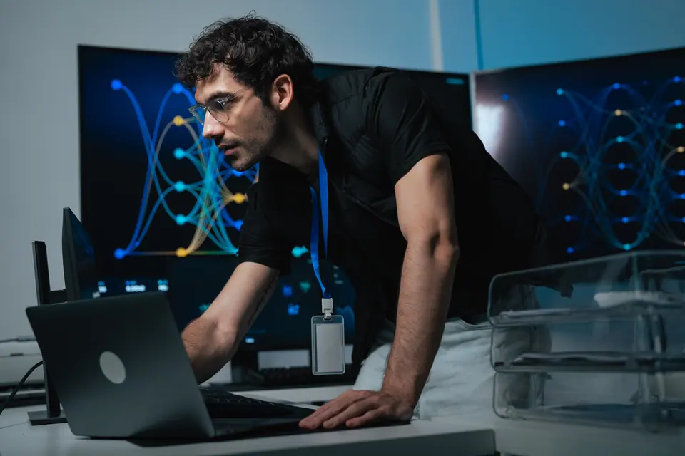 Programmer leans over laptop while working with software development, coding, artificial intelligence and computer data at technology workstation