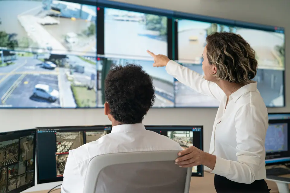 Rear view of female and male security coworkers discussing while looking and pointing at video wall in control room