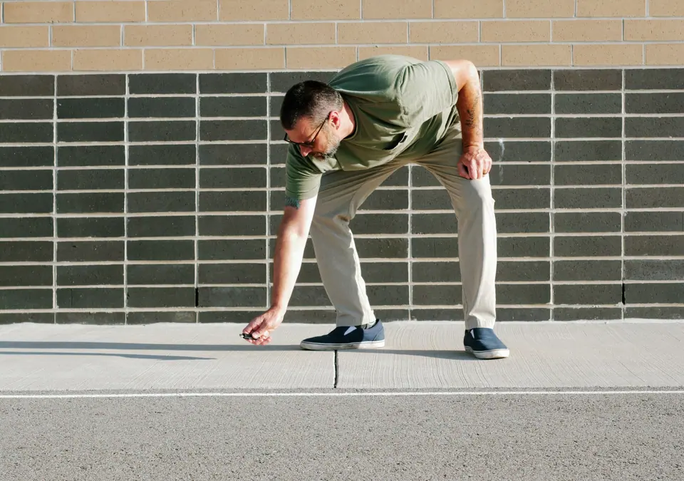 Unsuspecting man finds lost USB thumb drive on ground illustrating malicious USB drop attack - Cybersecurity Information Technology Concept