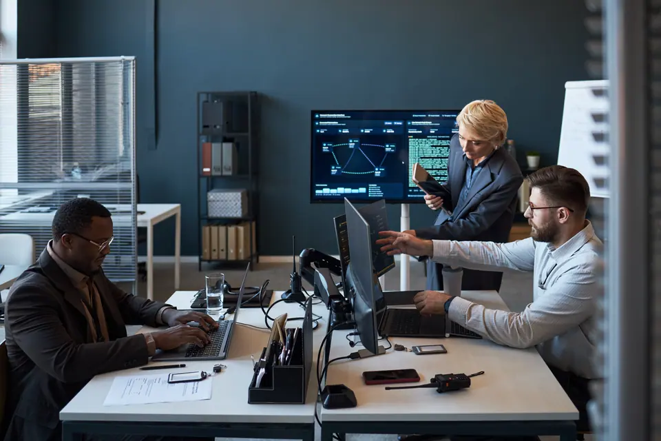 Wide shot of diverse business team reviewing data dashboards, coding, coordinating workflow in office