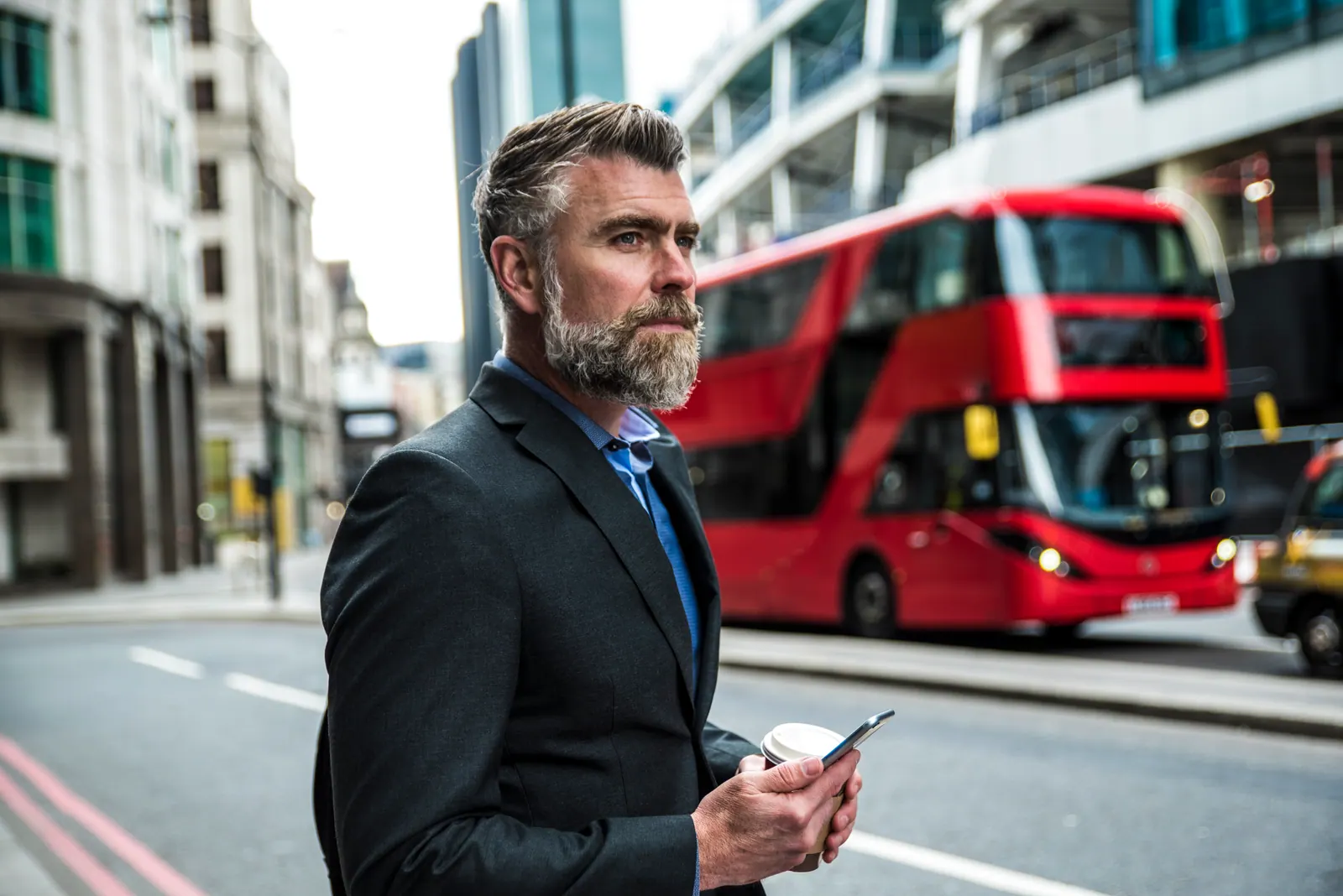 Man using a mobile phone on a city street beside a red bus