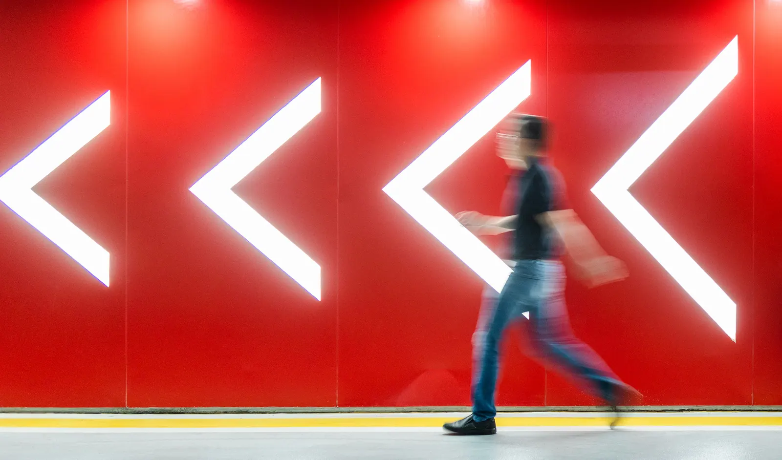 Person walking past illuminated arrows in a red corridor